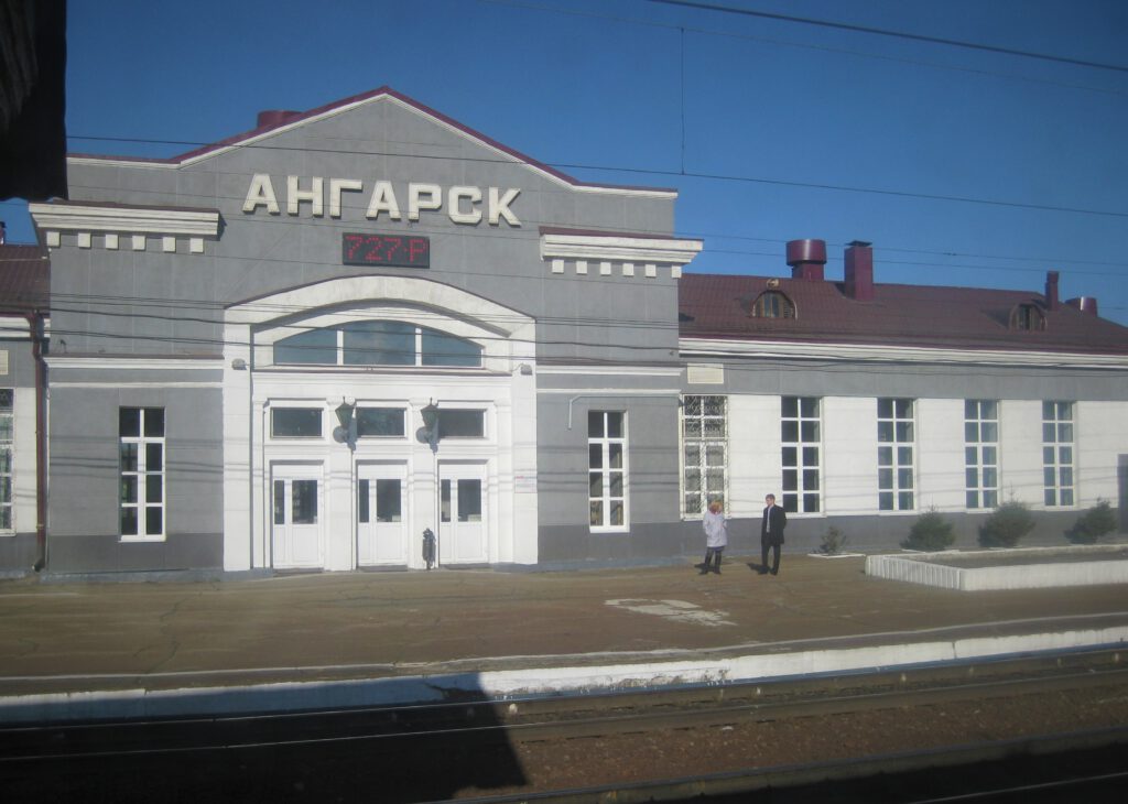 Vom Zug aus der Bahnhof von Angarsk in Sibirien. Zwei Leute stehen vor dem Gebäude. ангарск