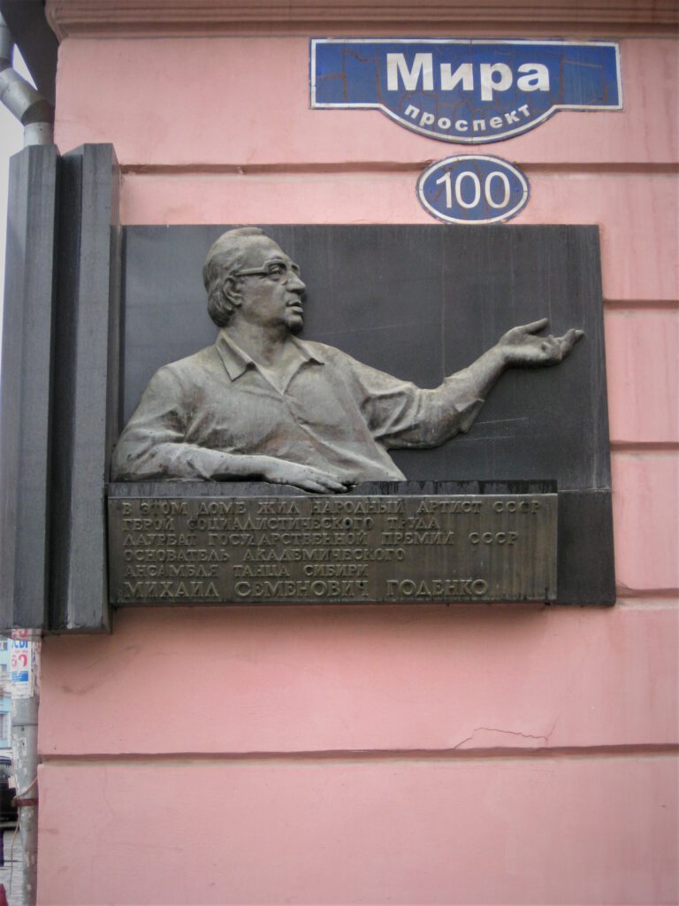 Bronze-Plakette an der Prospekt Mira 100 in Krasnojarsk. Andrey Pozdeev  reicht seine linke Hand elegant zur Seite. 

проспект мира