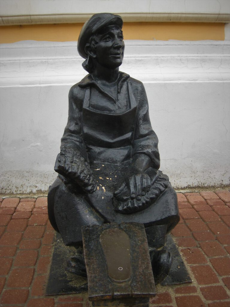 Skulptur einer sitzenden Schuhputzerin. 