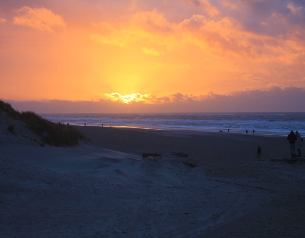 Sonnenuntergang hinter Wolken über Westküste von Texel. Im Vordergrund der Strand. 