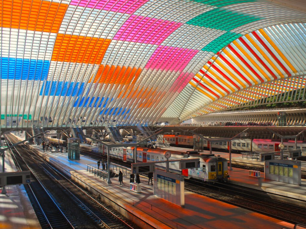 Im Bahnhof Liège-Guillemins schimmern Regenbogenfarben von bunten Quadraten des Dachs auf die Bahnsteige. 
