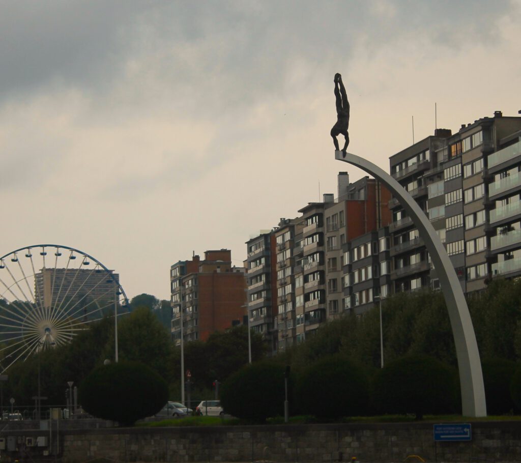 Rechts ragt die Bogen-Statue "Le Plongeur et son Arc" ins Bild. Ein Taucher im Handstand oben auf dem Bogen. Im Hintergrund ein Riesenrad.