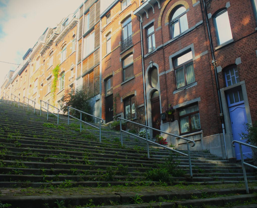 Mit Unkraut bewachsene, steile Treppe mit direkt angrenzenden Backstein-Wohnhäusern.