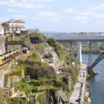 Regionalzug fährt entlang des Steilhangs von Porto. Im Hintergrund Brücken über den Douro.