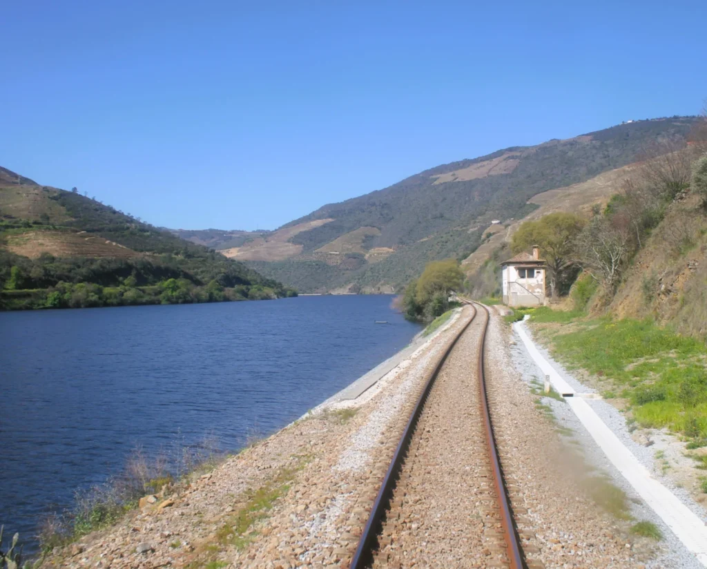 Gleisbett rechts neben dem blauen Douro-Fluss vor grünen Bergen. 
Aus dem Heckfenster für East Rail Stories.
