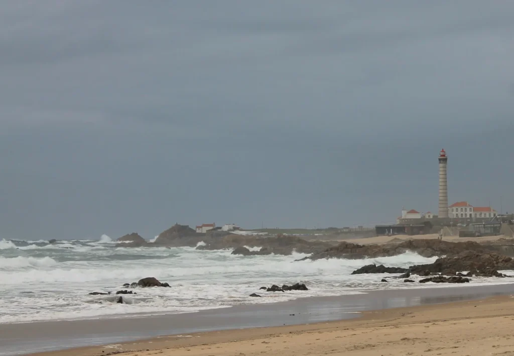 Strand und Felsküste von Leça da Palmeira mit Leuchtturm im Hintergrund.