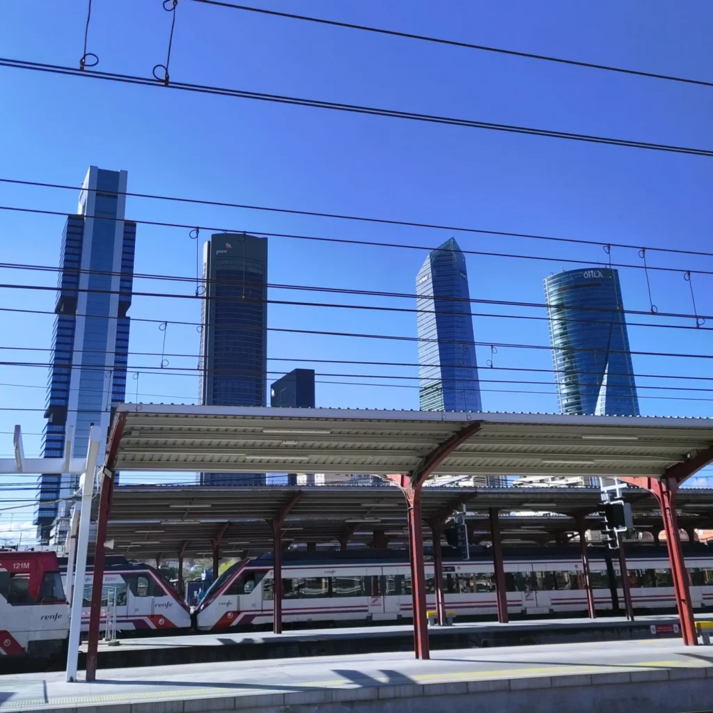 Vier Skyscraper vor den Bahnsteigen, mit einem Renfe Regionalzug.