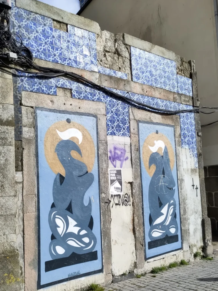Blaues Graffiti von Hazul an Mauer unter Azulejo Fassade. Abstrakte, vogelartig geschwungene Formen.