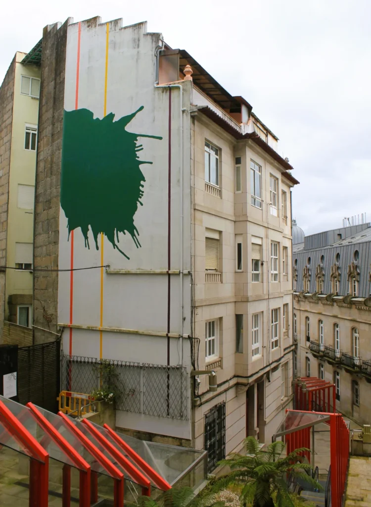 Hausfassade mit kunstvollem, grünen Klecks. Darunter überdachte Rolltreppen des Projekts "Vertical Vigo".