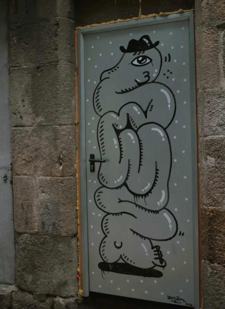 Graffiti-Bild eines stilisierten, vermenschlichten Dickdarms mit Hut auf grauer Stahltür.