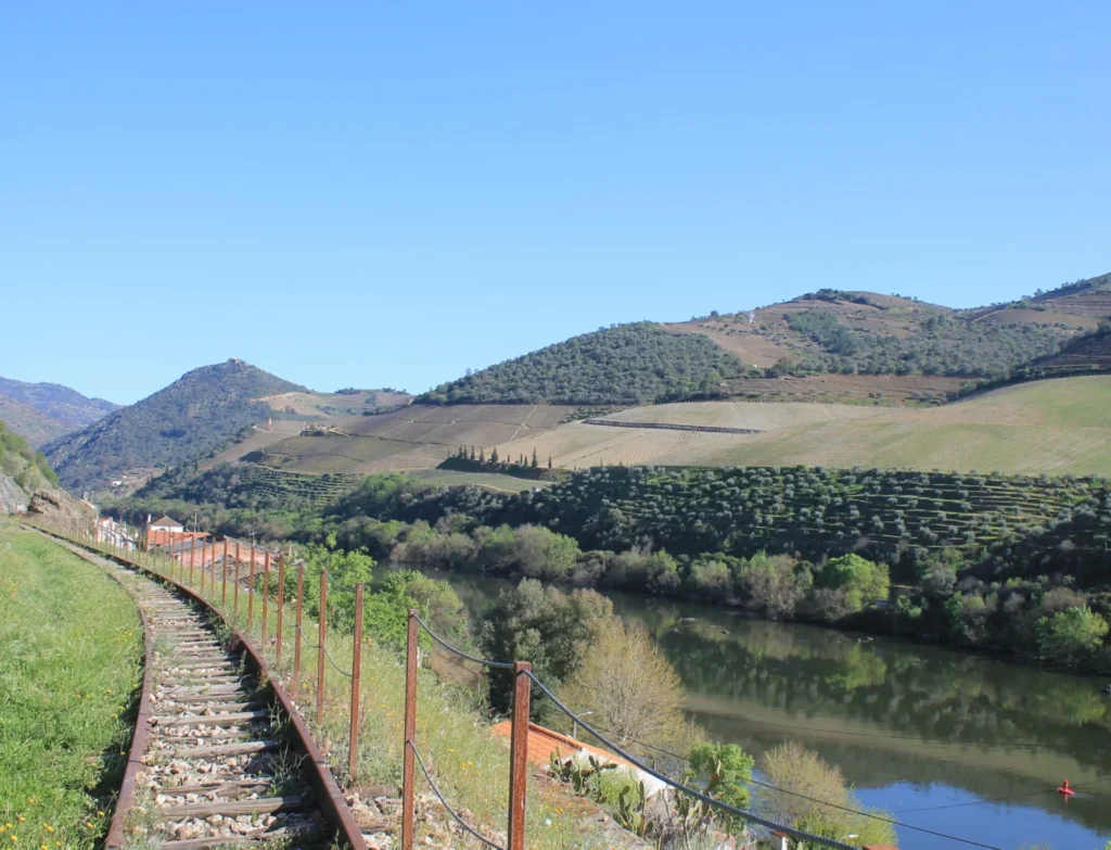 Gleisbett der Tua-Bahn links neben dem Douro-Fluss und der Hügellandschaft.