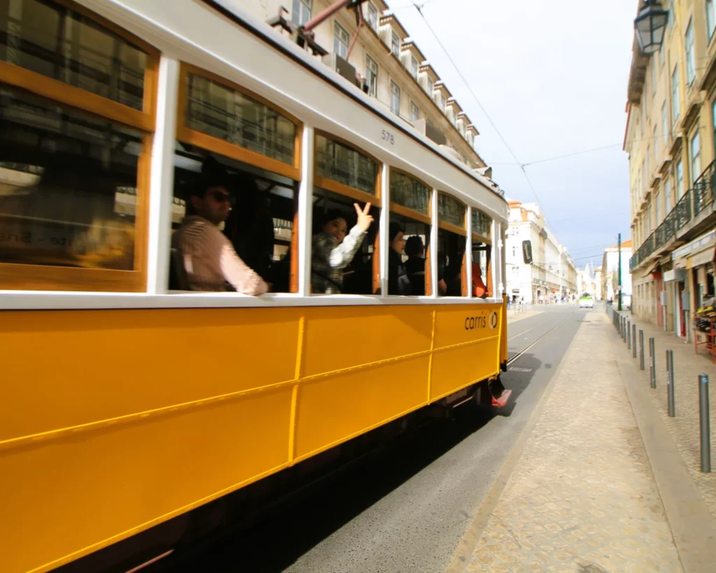 Vorbeifahrende Straßenbahn in Lissabon. Eine Frau winkt in die Kamera. 