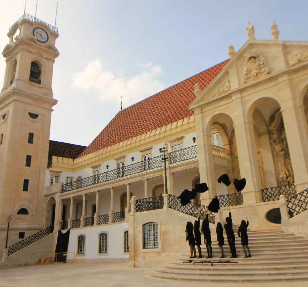 Coimbra Universität. Absolventinnen in schwarzer Montur werfen Roben vor dem Universitätspalast in die Höhe. 