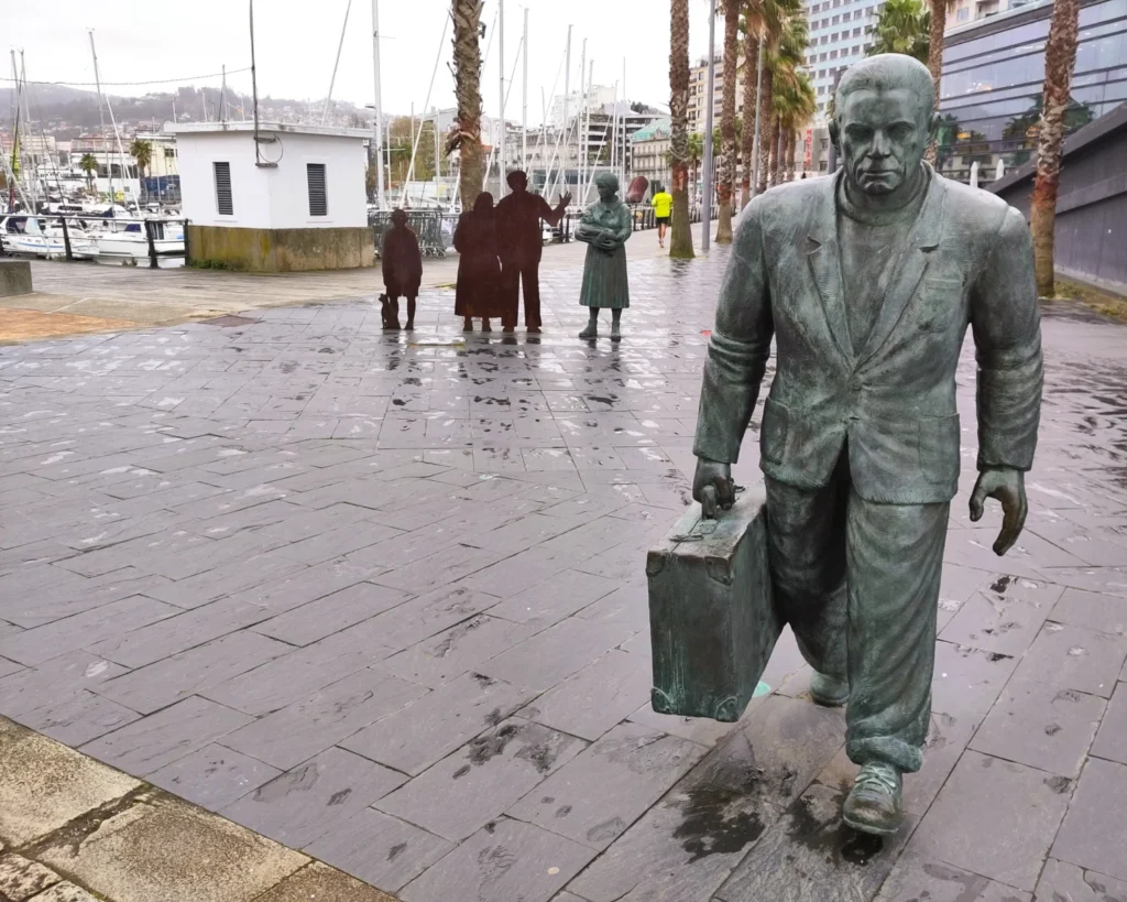 Bronzeskulptur eines Emigranten mit Koffer  am Hafen von Vigo. Dahinter Skulpturen seiner Familie. 