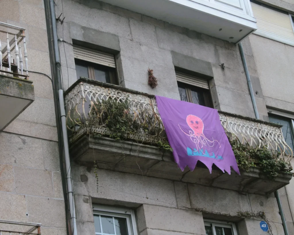 Balkon in Vigo, von dem ein lila Banner hängt. Darauf ist eine rosa Krake gemalt. 